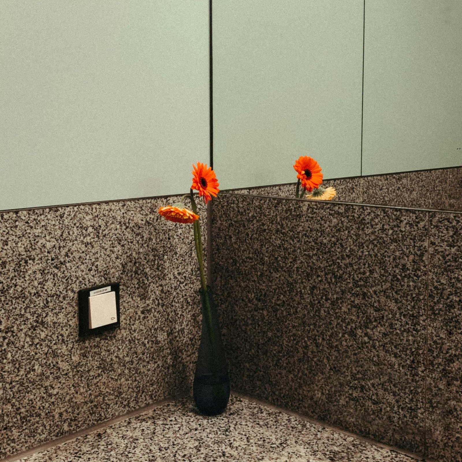 Stylish bathroom interior with vibrant orange gerbera daisies in a vase reflected in a mirror.